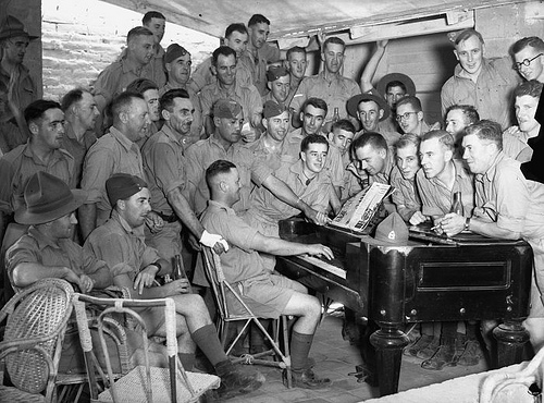 A large group of American WWII soldiers gathered around an old piano
